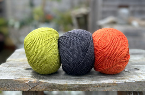 Three balls of yarn. From left to right - a green ball, a black ball and an orange ball