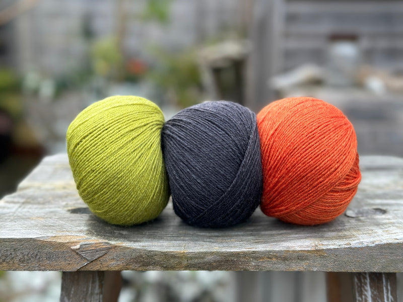 Three balls of yarn. From left to right - a green ball, a black ball and an orange ball