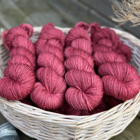 A white wicker basket containing several skeins of purpley-red yarn