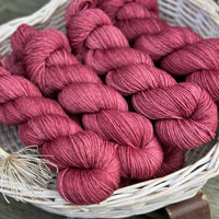 A white wicker basket containing several skeins of purpley-red yarn