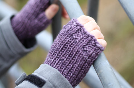 A person holding a metal fence and wearing purple fingerless mitts