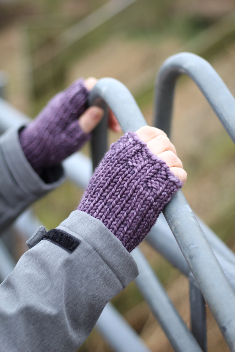 A person holding a metal fence and wearing purple fingerless mitts