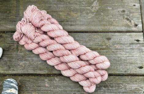 Five mini skeins of pink yarn with subtle gold sparkle running through it