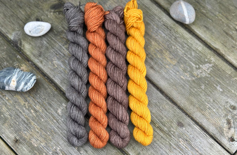 Four mini skeins. From left to right - a dark grey skein, a reddish brown skein, a brown skein and a deep yellow skein 