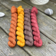 Four mini skeins. From left to right - a reddish brown skein, a deep yellow skein, a brown skein and a reddish purple skein