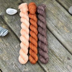 Three mini skeins. From left to right - a peachy orange skein, a reddish brown skein and a brown skein