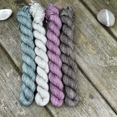 Four mini skeins. From left to right - a blue skein, a grey skein, a purple skein and a dark grey skein