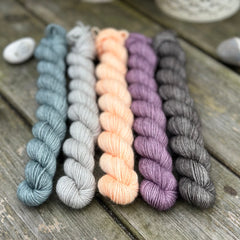 Five mini skeins of yarn - from left to right - a blue skein, a grey skein, a peachy orange skein, a purple skein and a dark grey skein