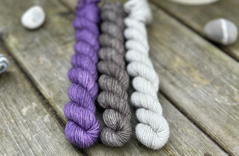 Three mini skeins of yarn in shades of purple and grey
