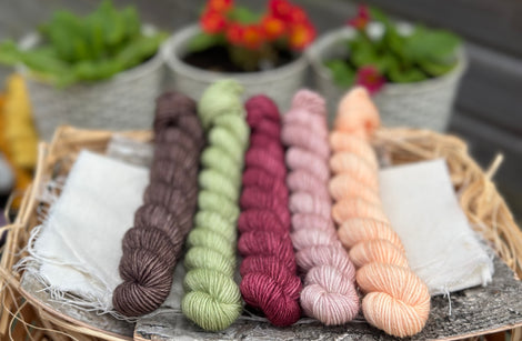 Five mini skeins of yarm. From left to right - a brown skein, a green skein, a reddish purple skein, a pink skein with gold sparkle running through it and a peachy skein
