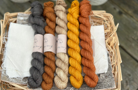 Five mini skeins of yarn in shades of black, brown and orange