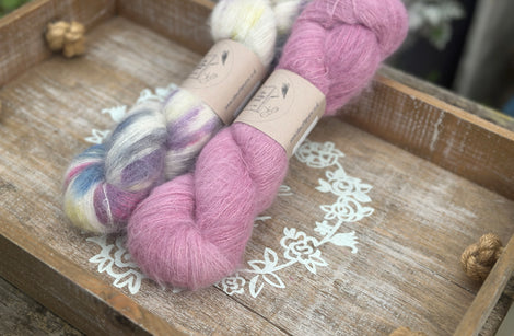 Two skeins of fluffy laceweight yarn - one variegated cream skein with multicoloured splashes and one pink skein