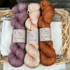 Three skeins of yarn. From left to right: a purple skein, a pale orange skein and an orangey brown skein