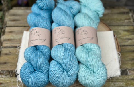 Three skeins of yarn in shades of blue with silver sparkle running through it
