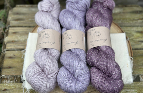 Three skeins of yarn in shades of purple with silver sparkle running through it