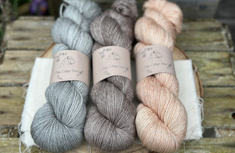 Three skeins of yarn with silver sparkle running through it. From left to right: a grey skein, a mid-brown skein and a pale orange skein