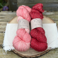 Two skeins of yarn with silver sparkle running through it. One skein is pink and one skein is red