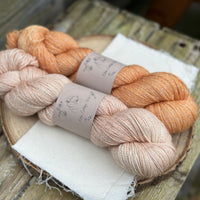 Two skeins of yarn with silver sparkle runnign through it. One pale orange skein and one orange skein
