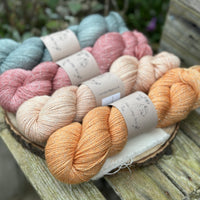 Four skeins of yarn with silver sparkle running through it. From left to right: a grey skein, a pink skein, a pale orange skein and an orange skein