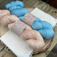 Two skeins of yarn with silver sparkle runnign through it. One pale orange skein and one blue skein