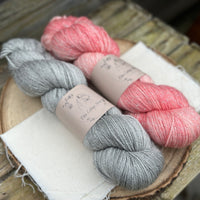 Two skeins of yarn with silver sparkle runnign through it. One grey skein and one pink skein