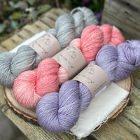 Three skeins of yarn with silver sparkle running through it. From left to right: a grey skein, a pink skein and a pale purple skein