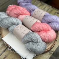 Three skeins of yarn with silver sparkle running through it. From left to right: a grey skein, a pink skein and a pale purple skein