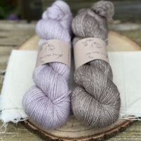 Two skeins of yarn with silver sparkle running through it. One pale purple skein and one mid brown skein