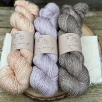 Three skeins of yarn with silver sparkle running through it. From left to right: a pale orange skein, a pale purple skein and a mid-brown skein
