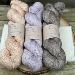 Three skeins of yarn with silver sparkle running through it. From left to right: a pale orange skein, a pale purple skein and a mid-brown skein