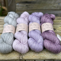 Four skeins of yarn with silver sparkle running through it. The colours fade from grey on the left to purple on the right