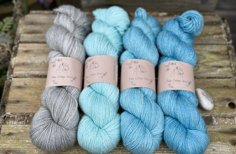 Four skeins of yarn with silver sparkle running through it. The colours fade from grey on the left to bright blue on the right