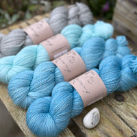Four skeins of yarn with silver sparkle running through it. The colours fade from grey on the left to bright blue on the right