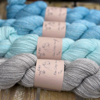 Four skeins of yarn with silver sparkle running through it. The colours fade from grey at the bottom to bright blue at the top