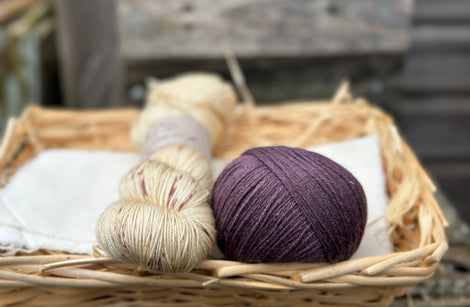 A skein of beige yarn with purple speckles with a ball of purple yarn
