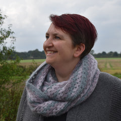 Victoria looking to the left of the image. She is wearing a grey cardigan and a fluffy granny stripe cowl in muted neutral tones
