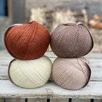 Four balls of yarn. Colours are natural cream, beige, reddish brown and brown