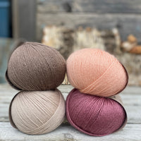 Four balls of yarn. Colours are beige, peach, purpley pink and brown