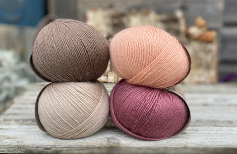 Four balls of yarn. Colours are beige, peach, purpley pink and brown