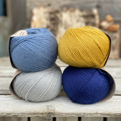Four balls of yarn. Colours are pale blue, blue, yellow and dark blue