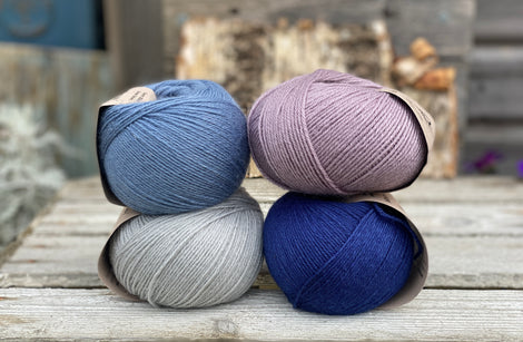 Four balls of yarn. Colours are pale blue, blue, pale purple and dark blue