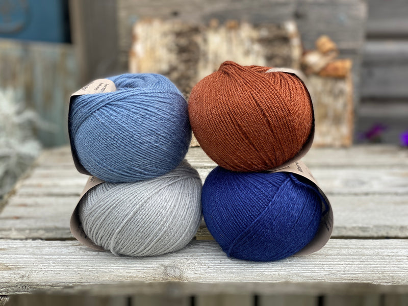 Four balls of yarn. Colours are pale blue, blue, reddish brown and dark blue