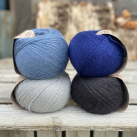 Four balls of yarn. Colours are pale blue, blue, dark blue and black