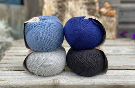 Four balls of yarn. Colours are pale blue, blue, dark blue and black