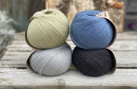 Four balls of yarn. Colours are pale blue, blue, pale green and black