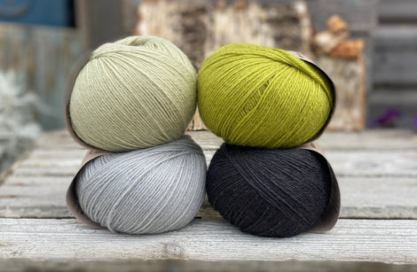 Four balls of yarn. Colours are pale blue, pale green, green and black