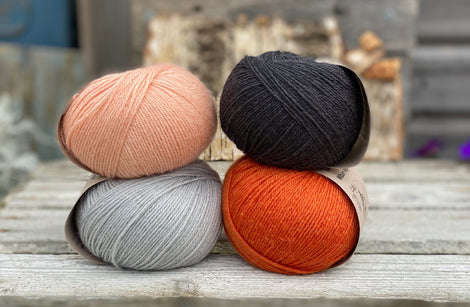 Four balls of yarn. Colours are pale blue, peach, orange and dark grey