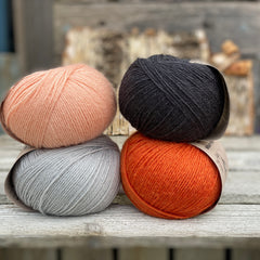 Four balls of yarn. Colours are pale blue, peach, orange and dark grey