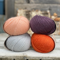 Four balls of yarn. Colours are pale blue, peach, orange and dark purple
