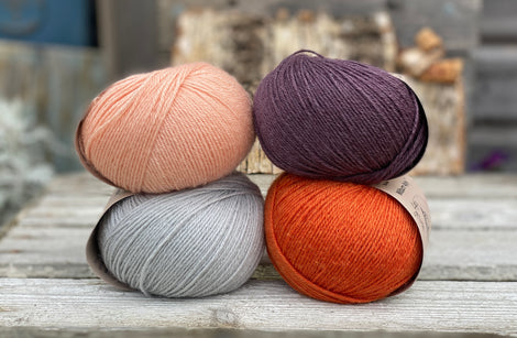 Four balls of yarn. Colours are pale blue, peach, orange and dark purple